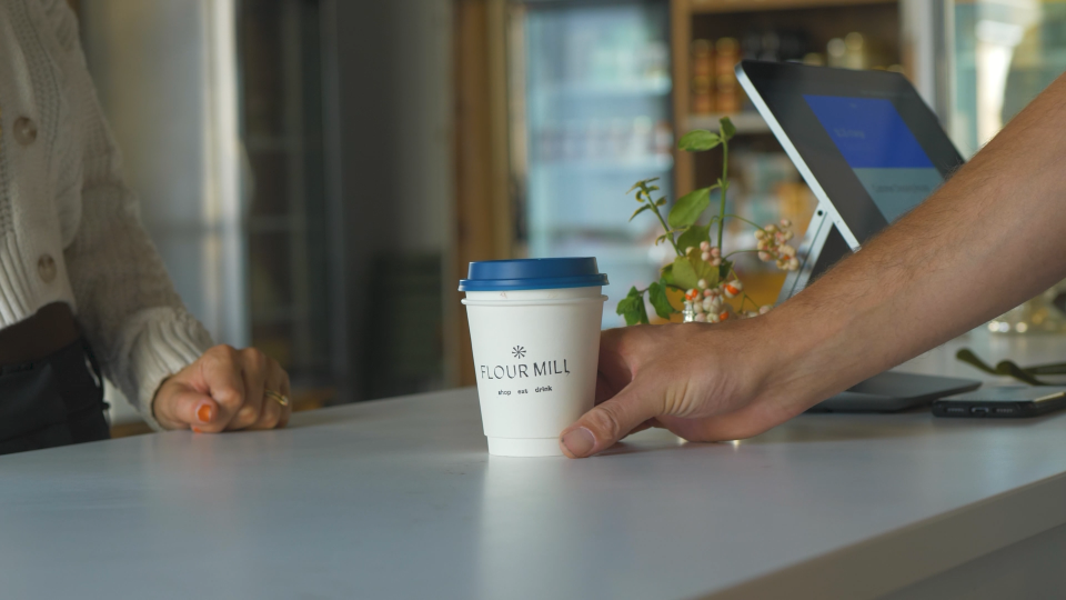 A person goes to grab their coffee order as it's passed to them on the counter