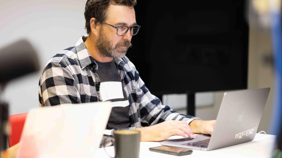 Jason looking at a laptop on a desk beside a coworker.