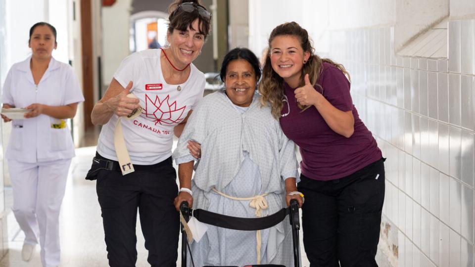 Photo of woman with a walker with two other women smiling and giving thumbs up