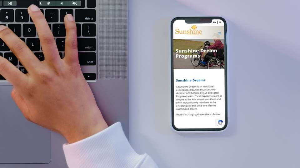 Sunshine Programs page visible on iPhone 11 while a person types on the computer