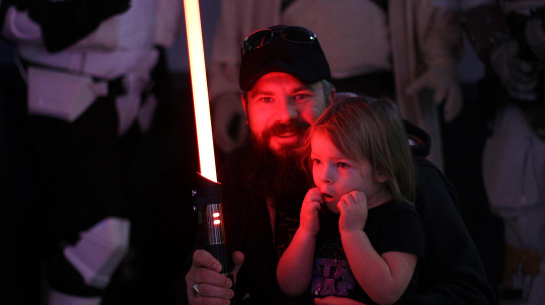 A man holding a red lightsaber and showing it to a fascinated child