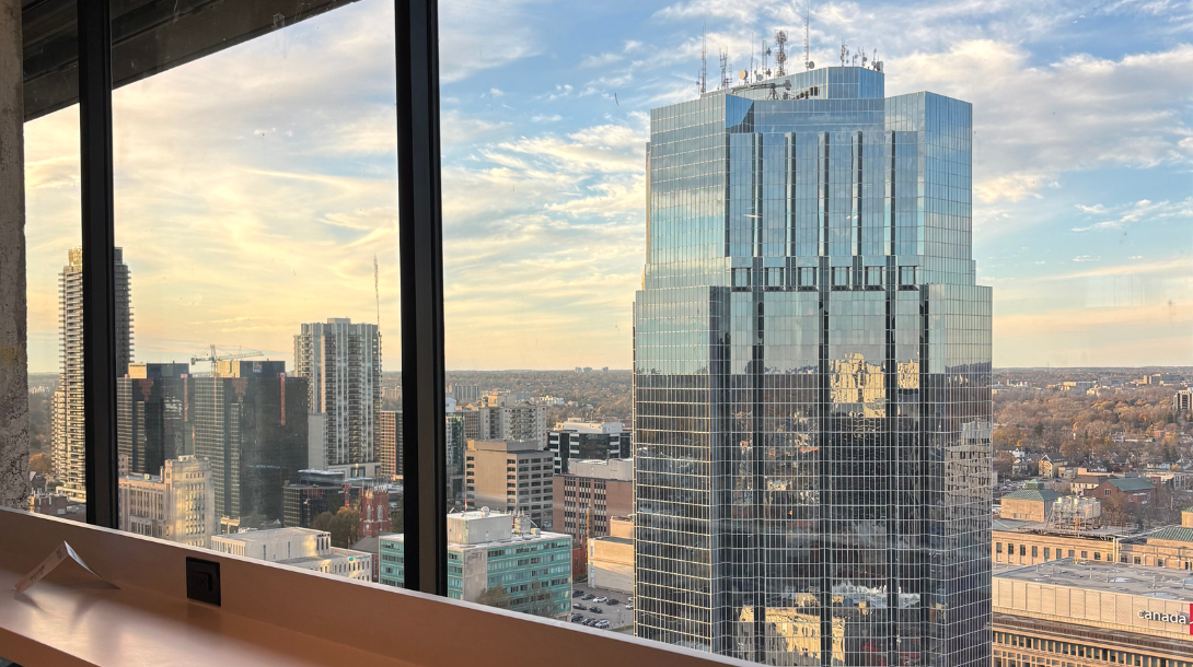 Looking out an office window to the horizon view of downtown London Ontario towards tall skyscrapers made of reflective glass.