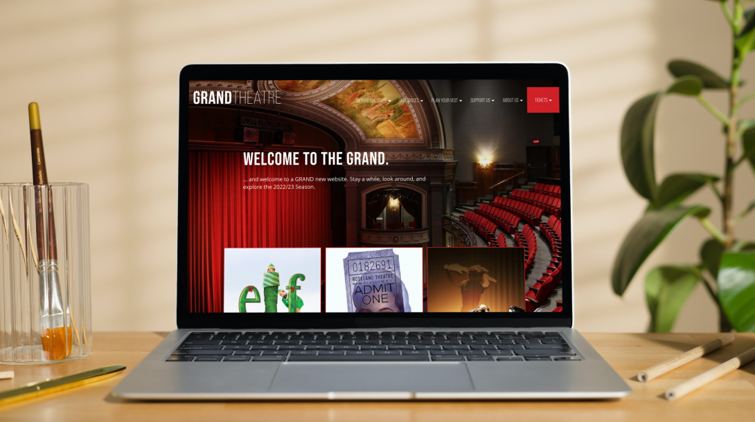 Macbook Air on a Wooden Desk with the Grand Theatre Website Open